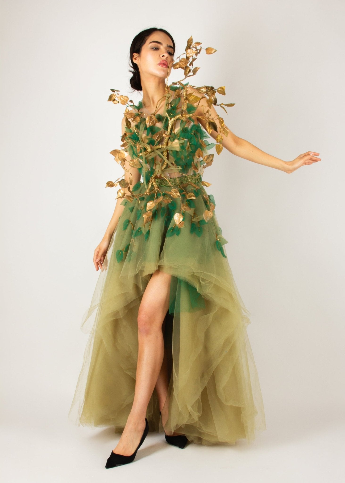 Enchanting nature-inspired gown by MNour Design, featuring a flowing olive-green tulle skirt with a high-low cut and an intricately designed bodice adorned with gold and green leaf appliqués. A breathtaking fusion of fashion and artistry. Discover this exclusive design at www.mnourdesign.com