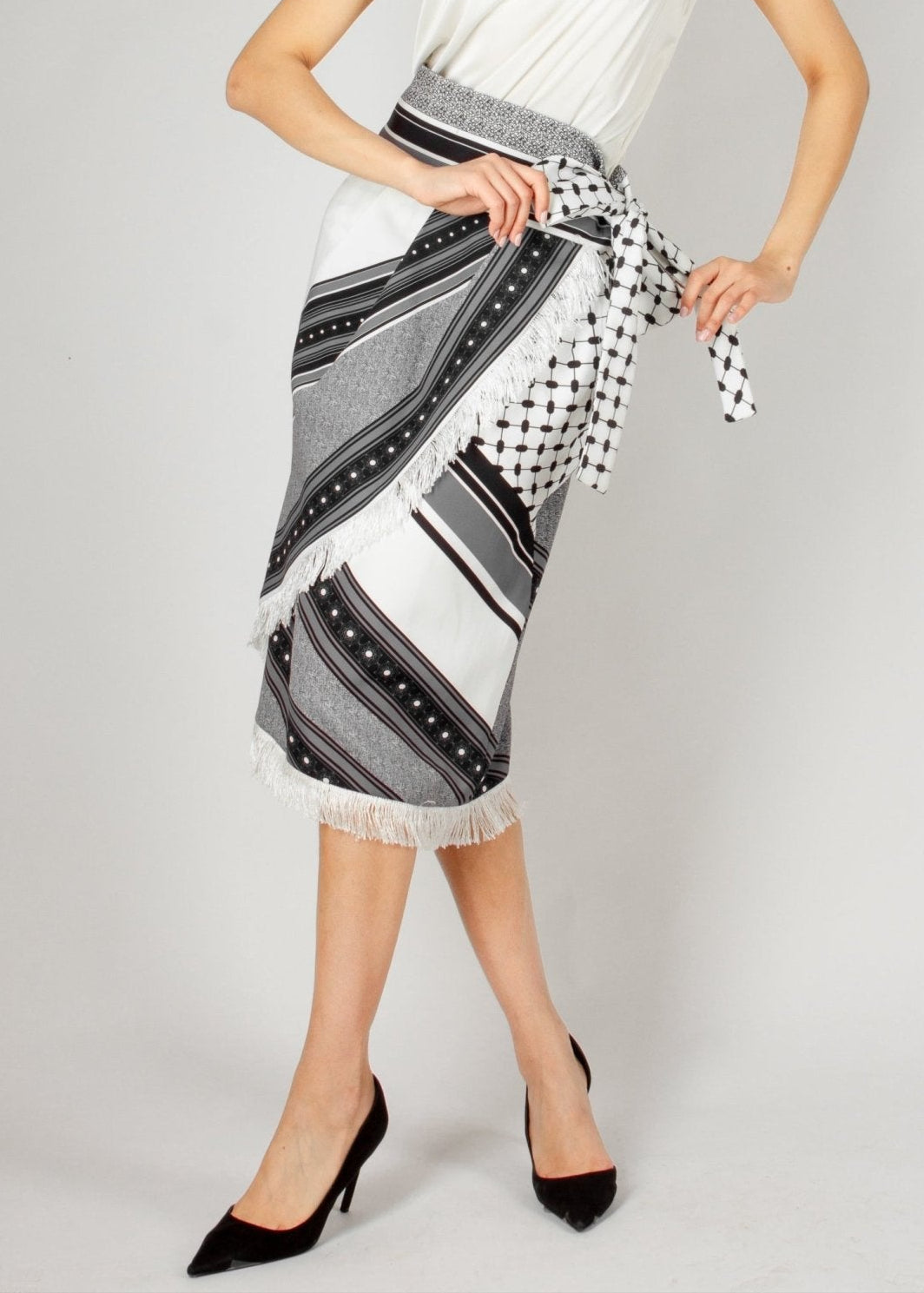 Chic wrap-style midi skirt from the HORRA collection by MNour Design, featuring a striking black-and-white traditional pattern with fringe detailing and a statement side tie. Paired with a sleek satin top and classic heels for an effortlessly elegant look. Explore more at www.mnourdesign.com
