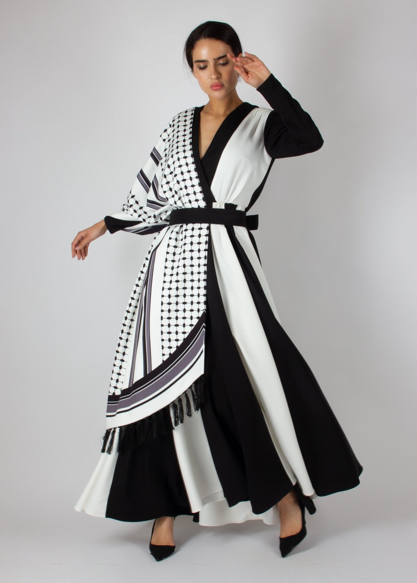 Flowing black and white wrap dress from the HORRA collection by MNour Design, featuring keffiyeh-inspired prints and elegant fringe details. A statement piece blending cultural heritage with modern sophistication. Discover more at www.mnourdesign.com