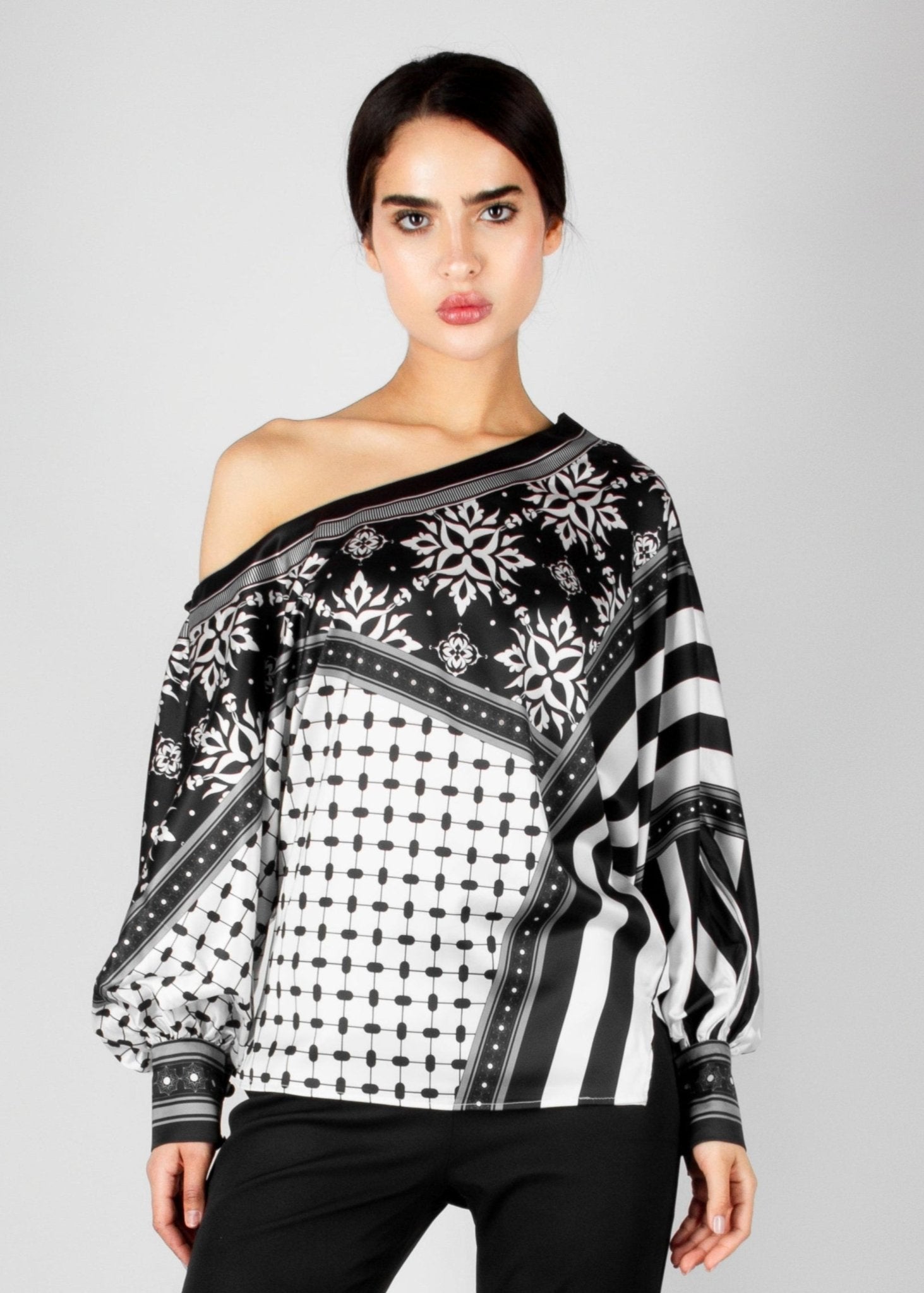 Bold off-shoulder blouse from the HORRA collection by MNour Design, featuring a striking keffiyeh-inspired pattern with intricate geometric details. Paired with sleek black trousers for a modern, sophisticated look. Explore more at www.mnourdesign.com