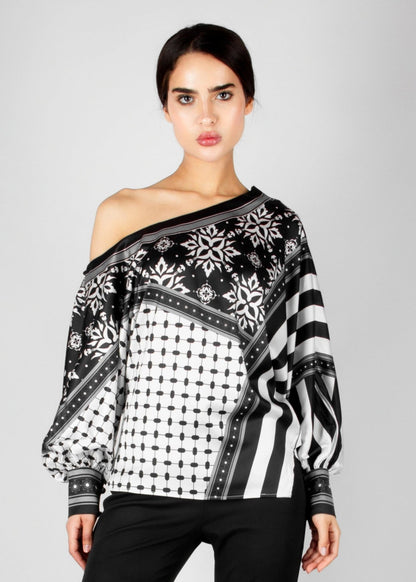 Bold off-shoulder blouse from the HORRA collection by MNour Design, featuring a striking keffiyeh-inspired pattern with intricate geometric details. Paired with sleek black trousers for a modern, sophisticated look. Explore more at www.mnourdesign.com